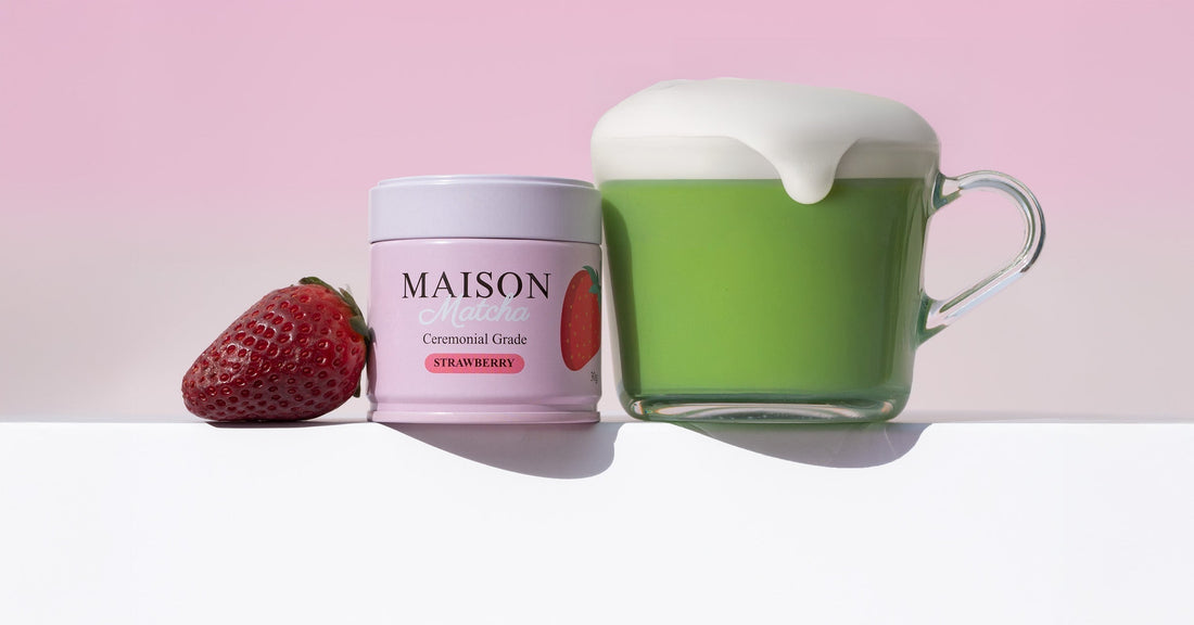 Cup of frothy strawberry matcha latte with Maison Matcha Strawberry can and fresh strawberry on the side