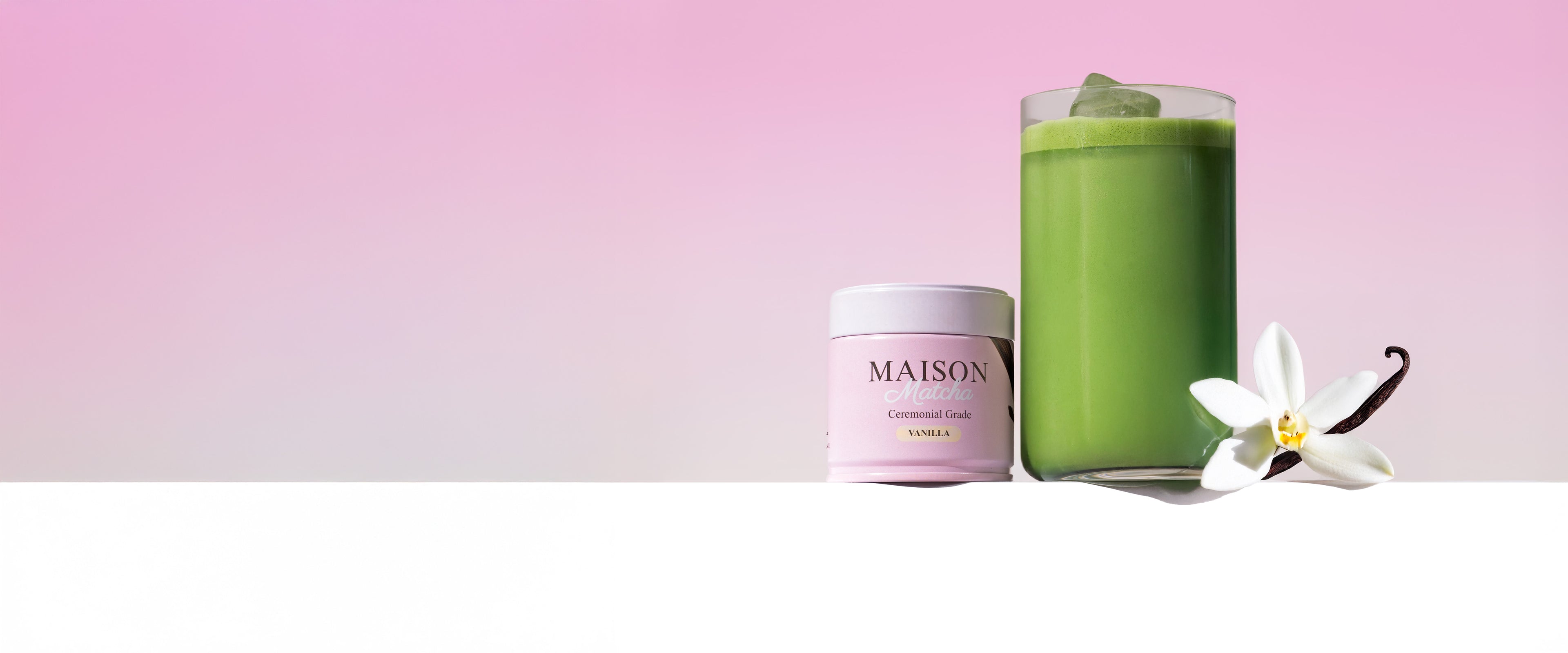 Maison Matcha Ceremonial Vanilla Matcha can beside iced matcha latte, garnished with vanilla flower and vanilla bean