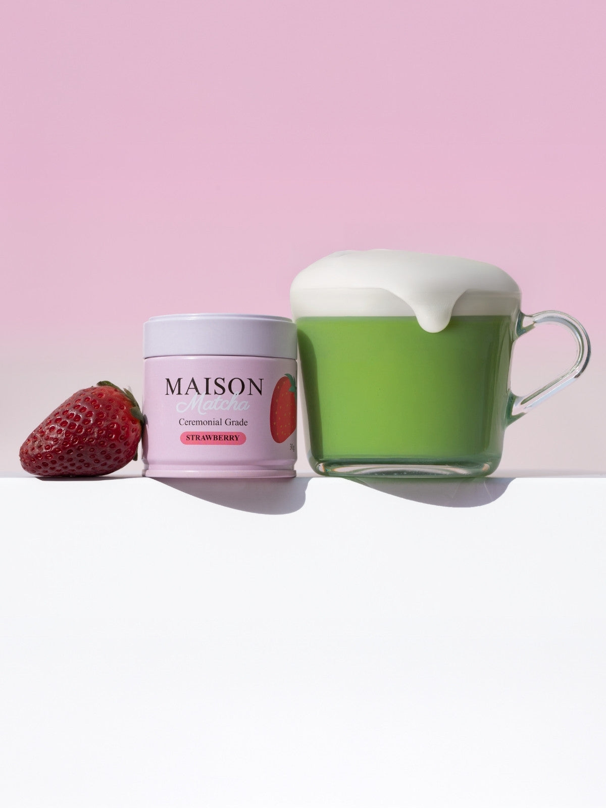 Dripping hot ceremonial Strawberry Matcha latte with can and fresh strawberry on table